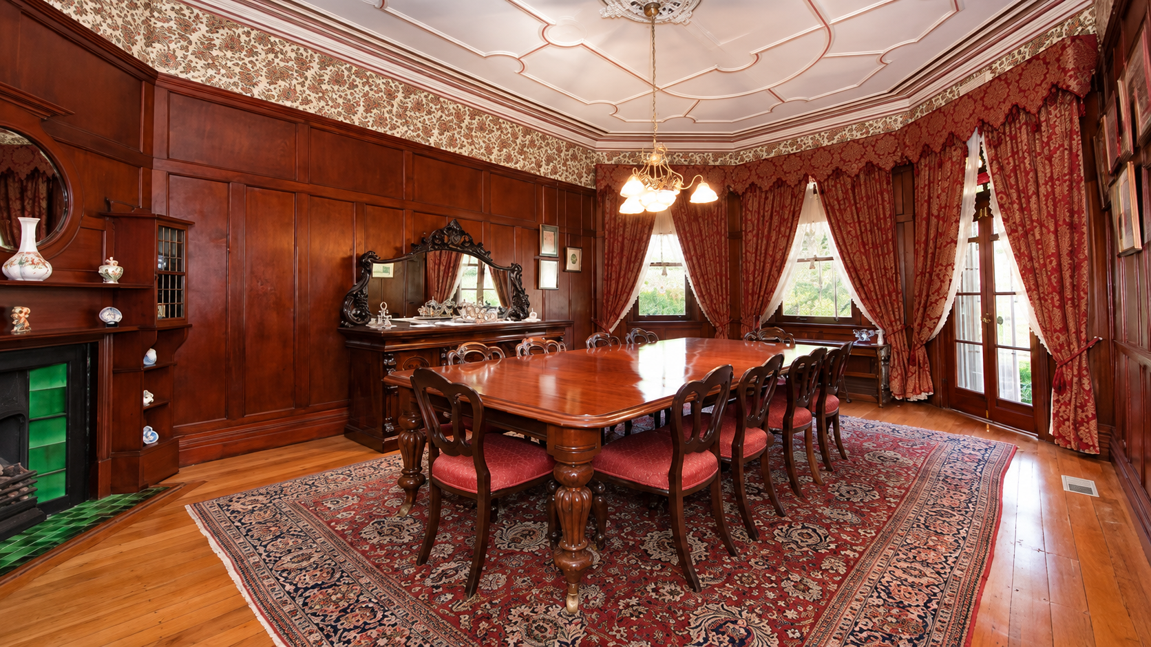 Elegant wood-paneled dining room with long table, patterned rug, and red curtains by tall windows