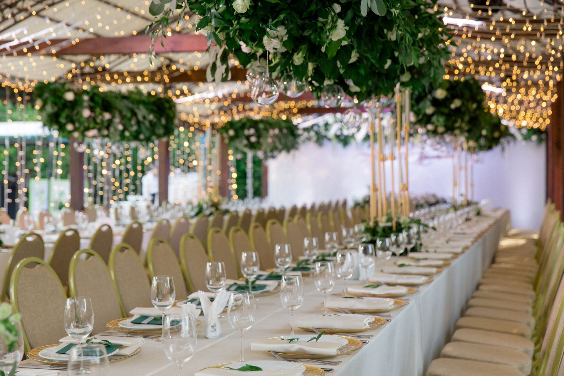 A long table set for a wedding reception with plates , glasses , and flowers hanging from the ceiling.