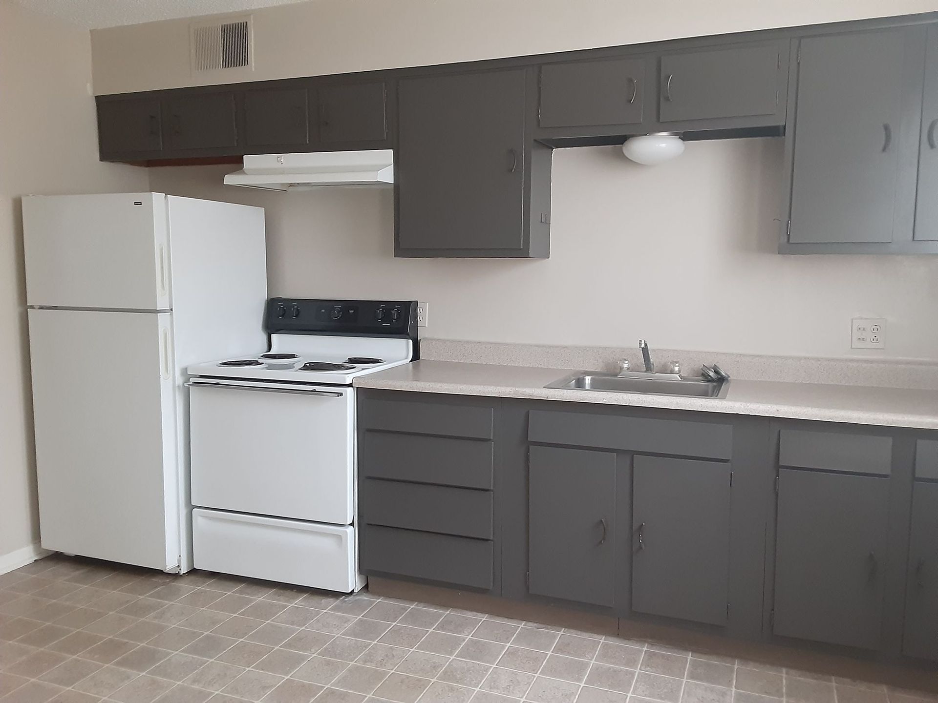 Kitchen with white appliances, gray cabinets, and a beige countertop.