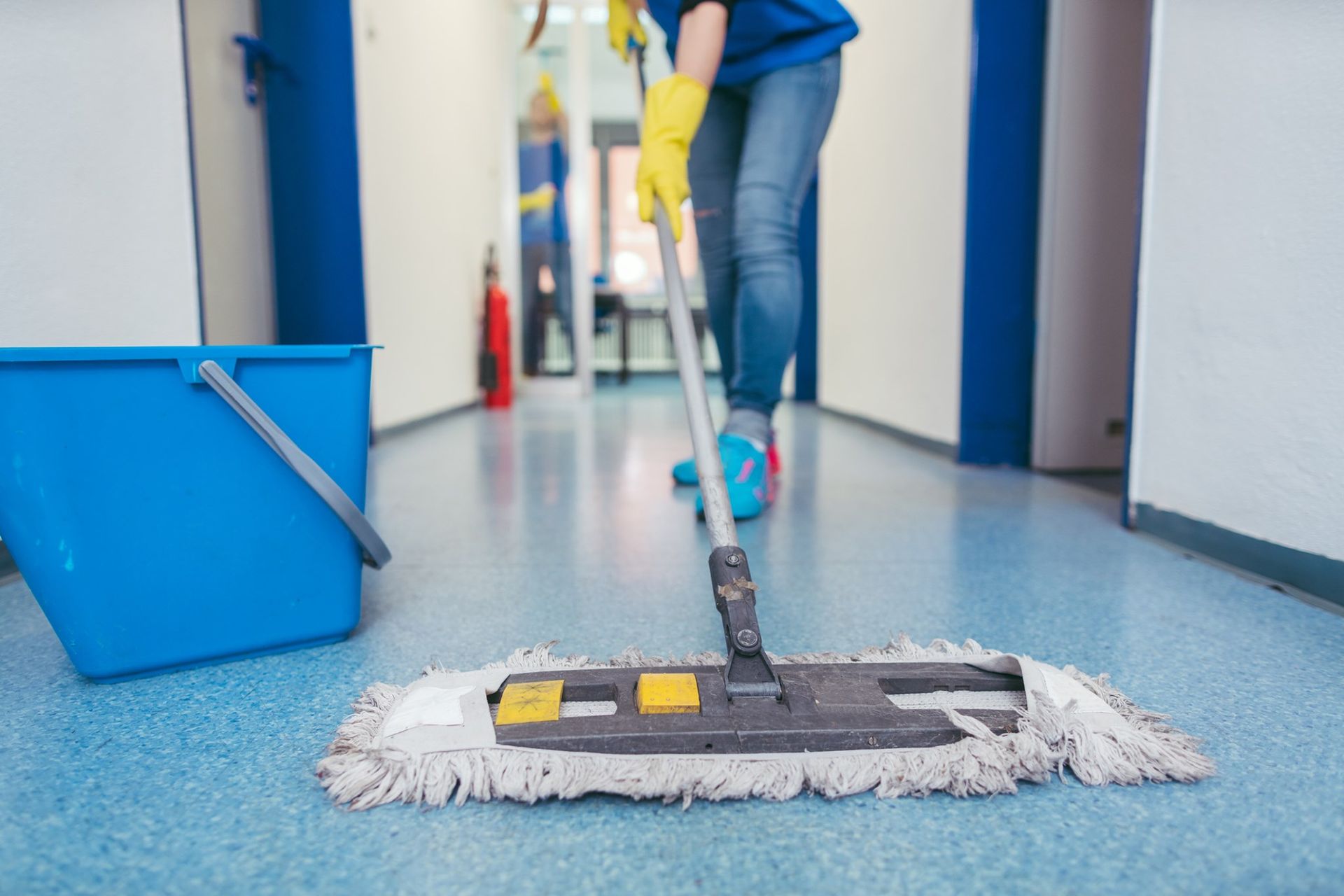 A woman is cleaning the floor with a mop in a hallway.
