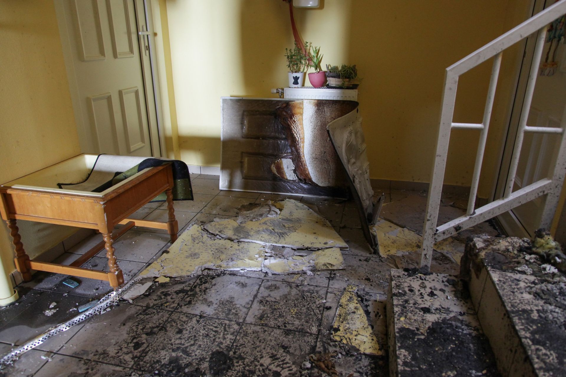 A room with fire damage to the stairs and has a table in it