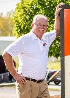 A man in a white shirt and khaki pants is leaning against a sign.