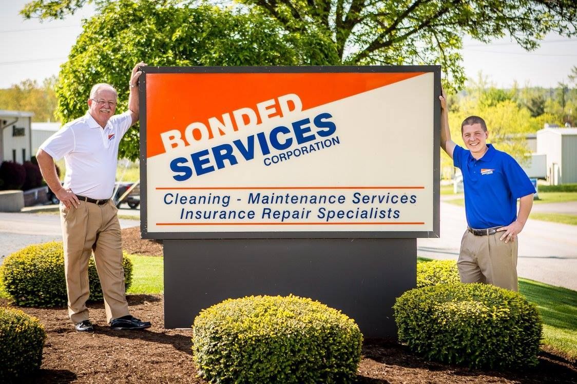 Two men standing next to a sign that says bonded services