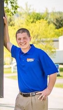 A man in a blue shirt and khaki pants is leaning against a pole.