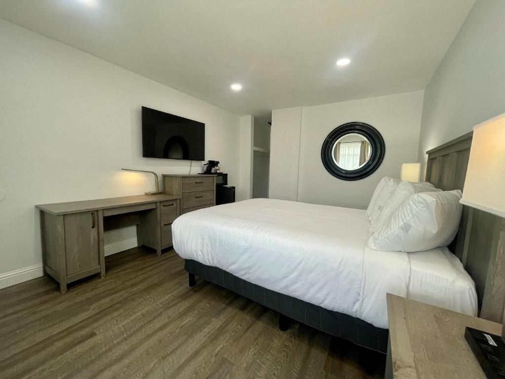 A hotel room with a king size bed , desk , television and mirror.