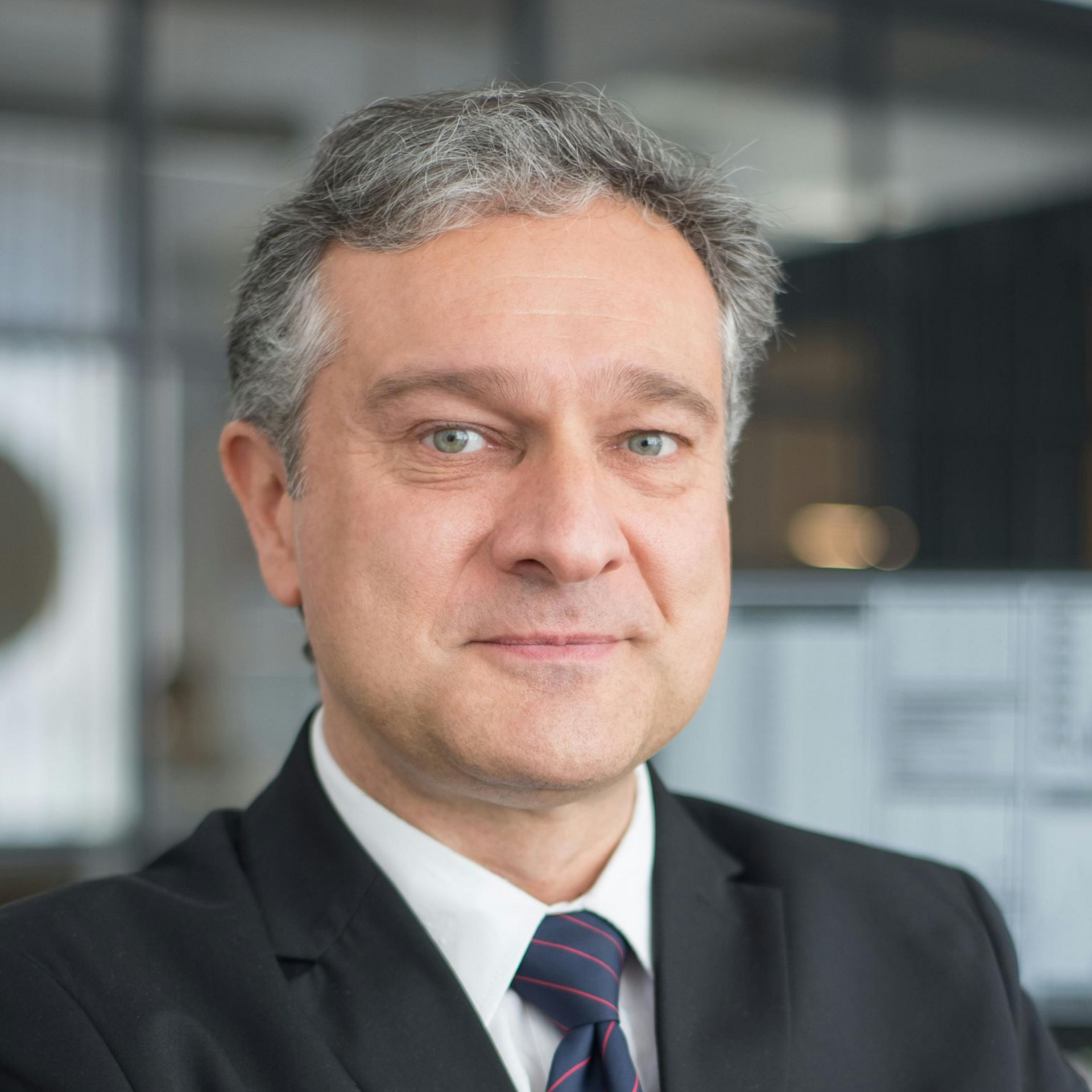 Man in suit and tie, smiling, indoors.