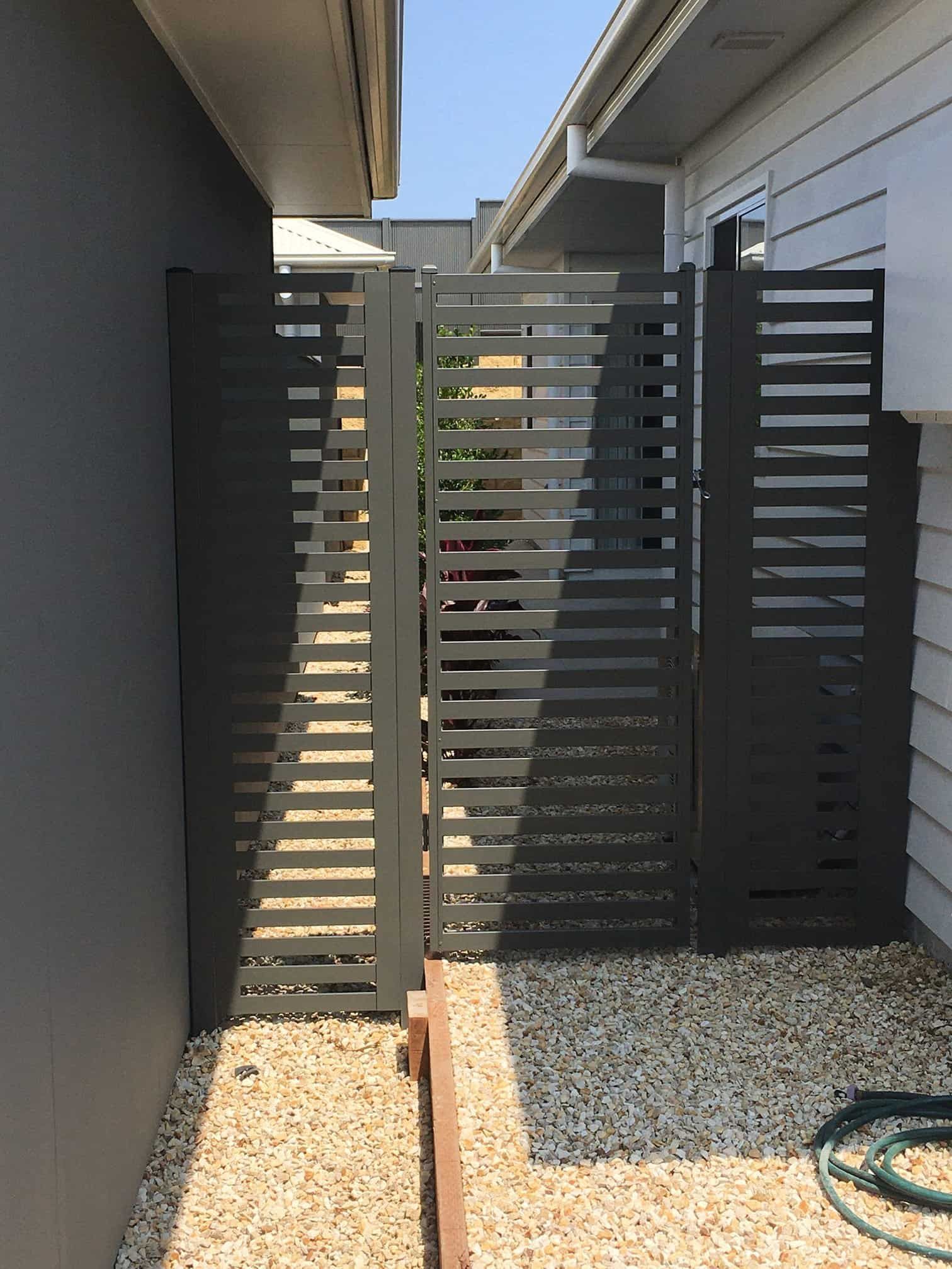 A Fence With A Hose Next To It Is Between Two Houses — Australian Advanced Fencing In Port Macquarie, NSW