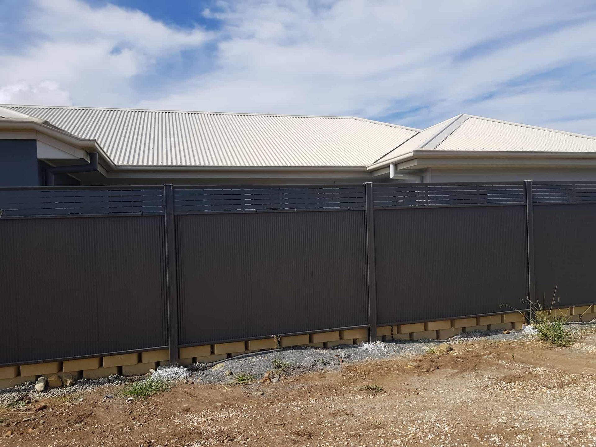 A Black Fence Is In Front Of A House With A White Roof — Australian Advanced Fencing In Port Macquarie, NSW