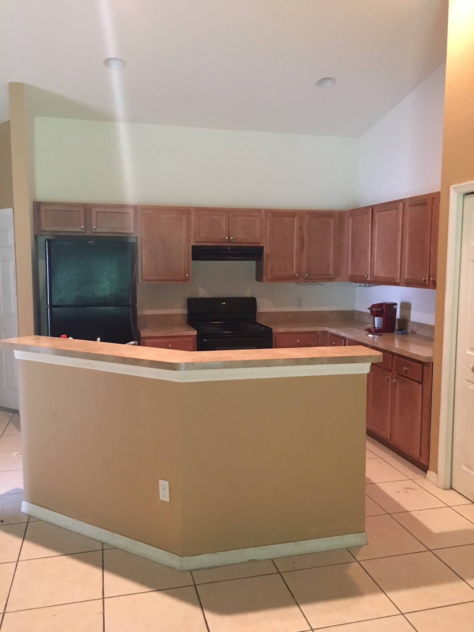 Empty kitchen with wood cabinets, black appliances, and a tan island with white trim.