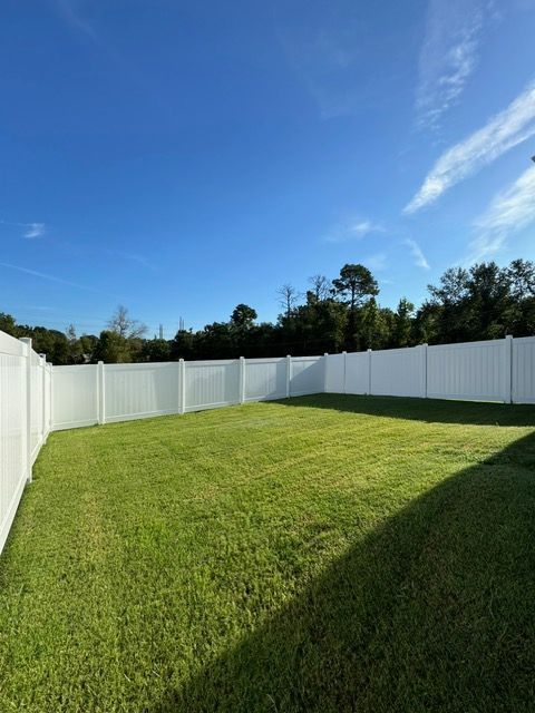 Sunny backyard with a white privacy fence, green lawn, and blue sky with a few clouds.