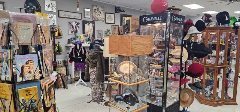 Cluttered vintage shop with hats, clothes, art, and shelves of antiques on display