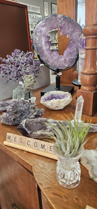Crystal display with purple geodes, a quartz ring, and a small “WELCOME” sign on a wooden stand.