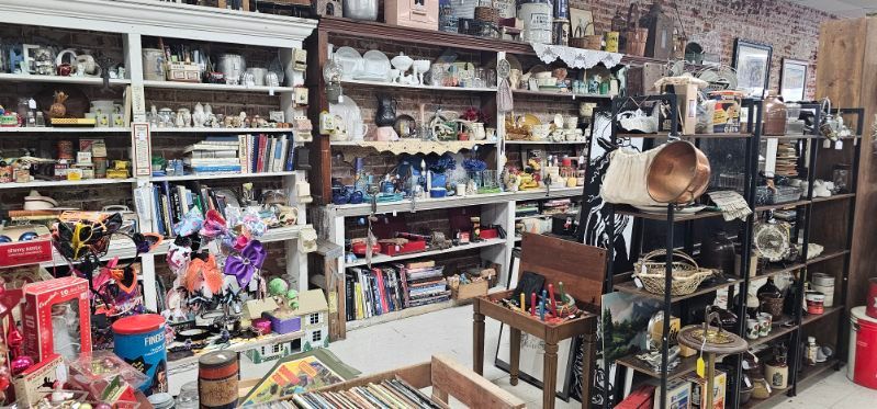 Crowded antique shop aisle with shelves of assorted collectibles, lamps, and vintage items
