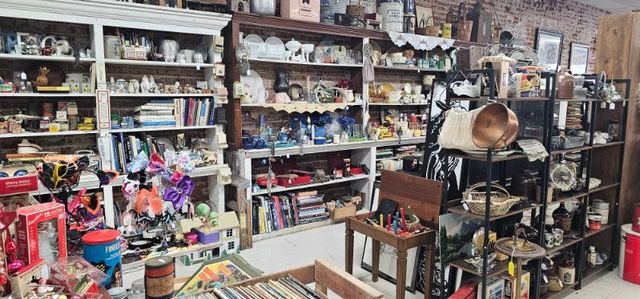 A colorful antique shop interior filled with retro decor, weird finds, rock shop items, costumes, vintage clothing, hats, and magazine racks.