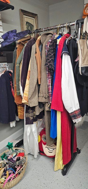 Clothes hanging on a rack in a small room, with colorful garments and shoes stored below.