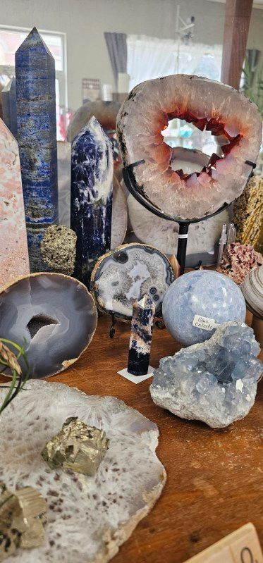 Assortment of crystals and geodes displayed on a wooden table, including large amethyst and quartz pieces.