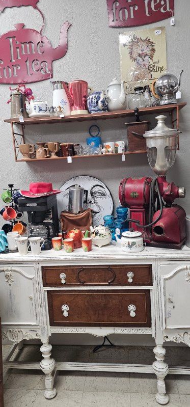 Vintage-style display of teapots, mugs, and kitchen decor on a white cabinet and shelves