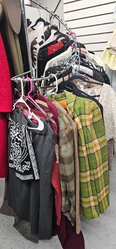 Clothing rack with assorted jackets and shirts in red, black, green, and plaid patterns indoors