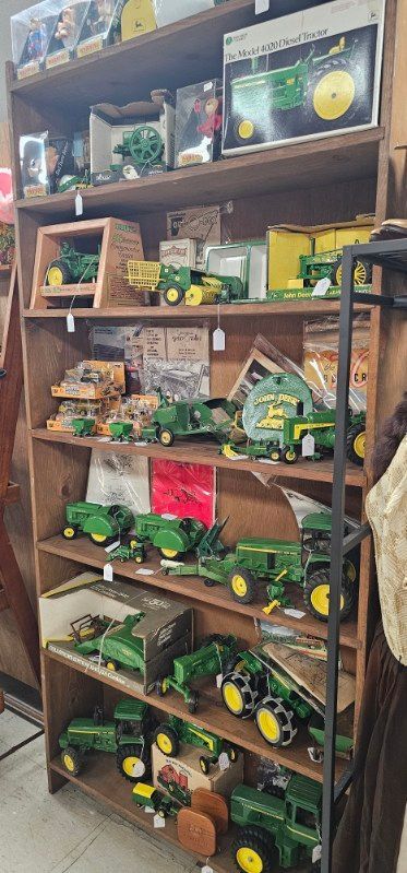 Wooden shelf display of green toy tractors, farm items, and yellow wheels in a shop or market stall