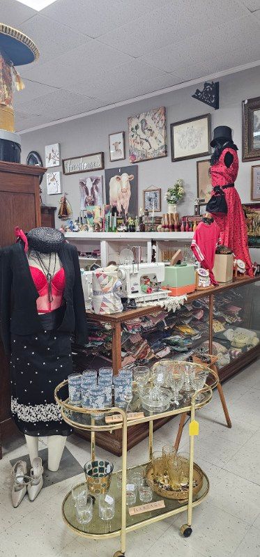 Thrift store display with mannequins in colorful clothing, jewelry cases, and framed art on the walls