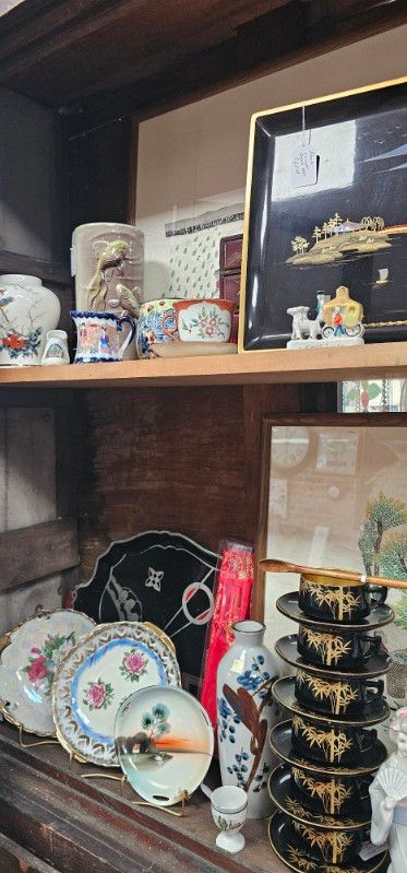 Wooden shelf displaying porcelain plates, teacups, and decorative figurines in a dim room.