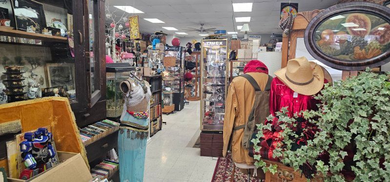 Cluttered antique shop aisle with shelves, hats, dolls, and vintage decor