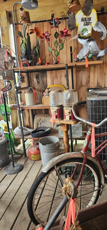 Bicycle in a cluttered rustic workshop with hanging tools, shelves, and containers on wooden flooring