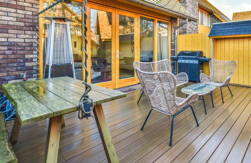Backyard wooden deck with wicker chairs, glass table, grill, and house windows