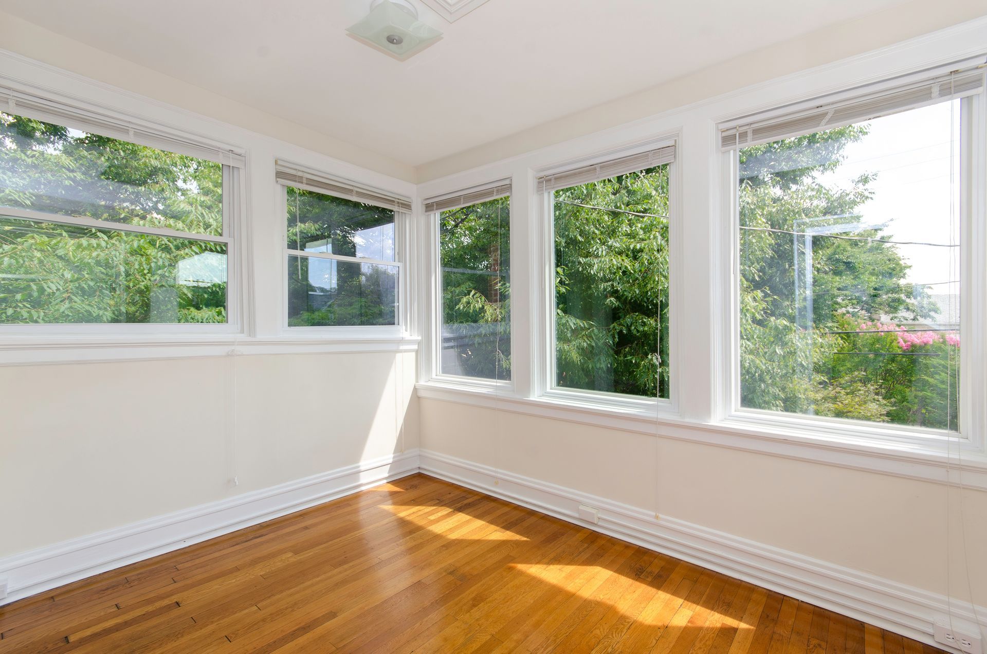 Bright empty room with white walls, large windows, and sunlit hardwood floors