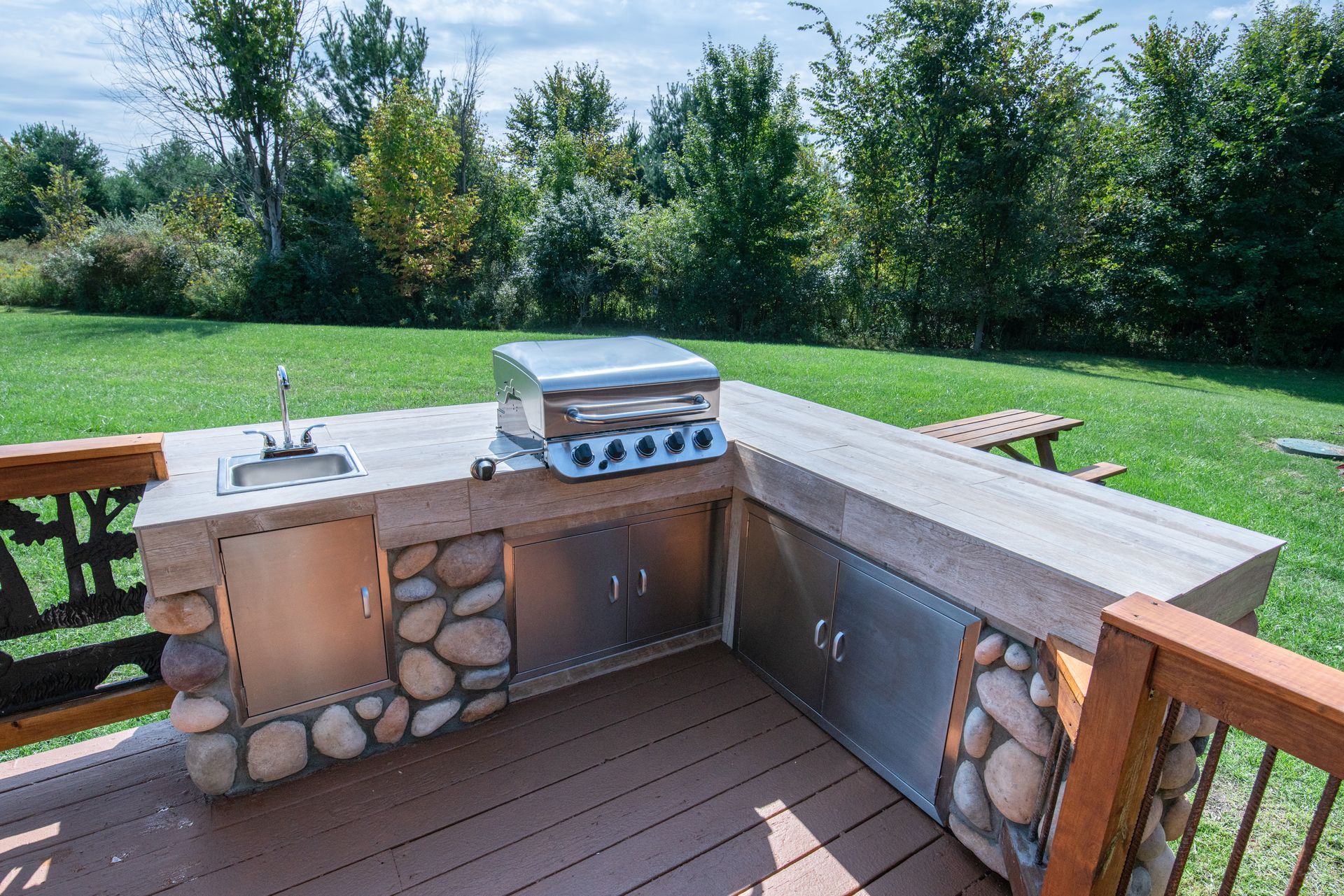 Outdoor stone patio with built-in grill, sink, and cabinets overlooking a grassy backyard