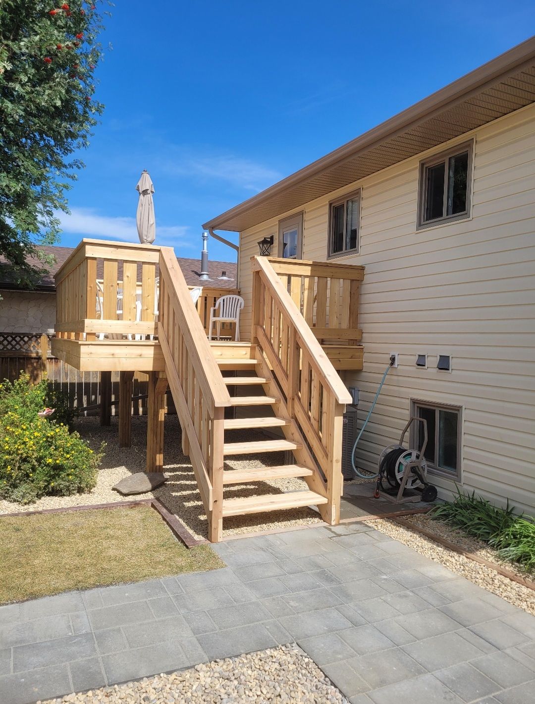 A wooden deck with stairs leading up to it is in the backyard of a house.