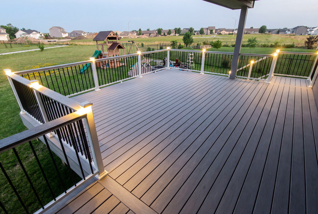 Wooden deck with white railings overlooking a green neighborhood at sunset