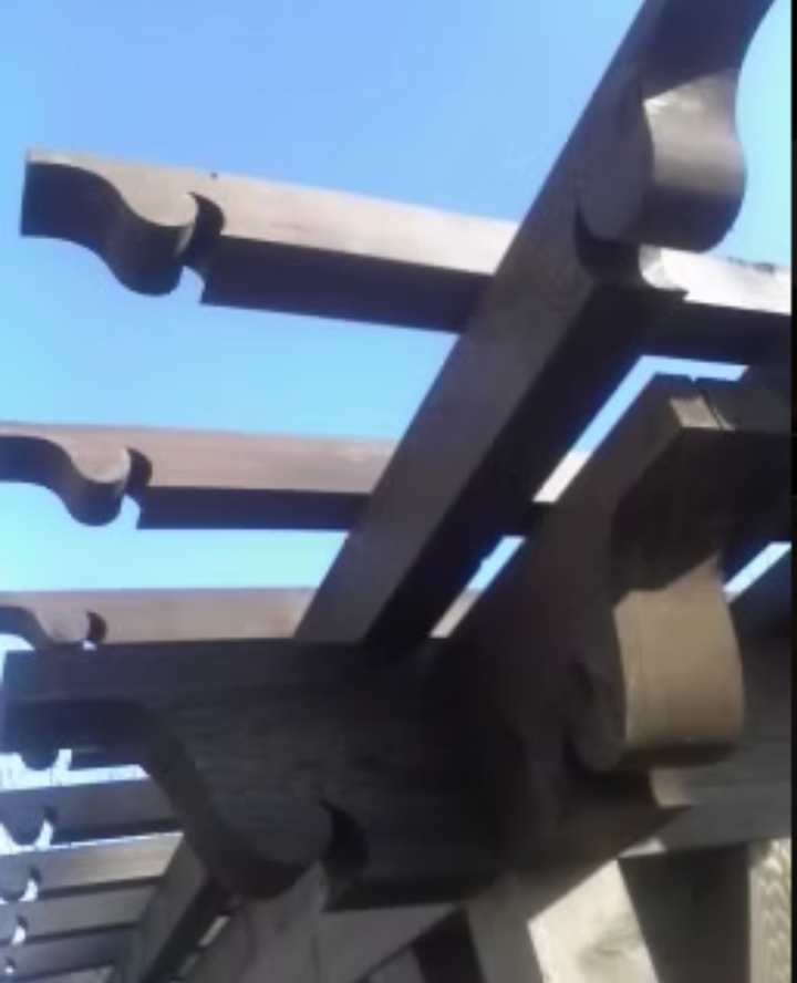 Close-up of dark wooden pergola beams against a bright blue sky.