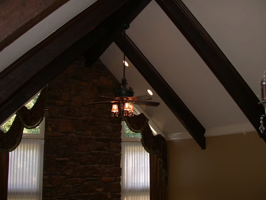 Interior with exposed dark wood ceiling beams, hanging chandelier, and windows with draped curtains