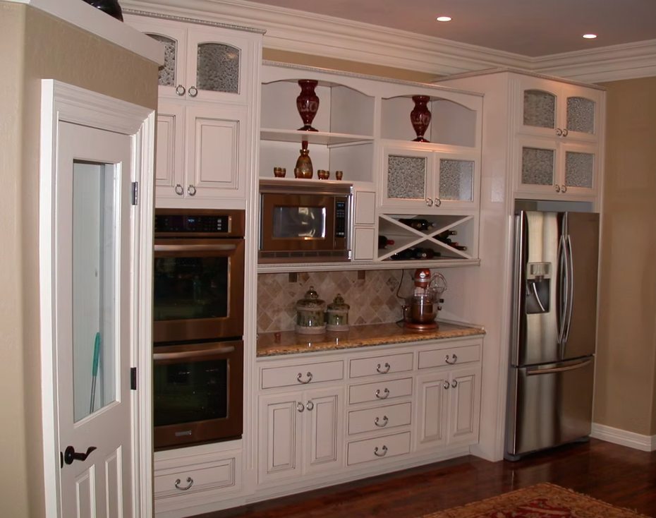 White kitchen with built-in appliances, glass cabinets, and a stainless steel refrigerator