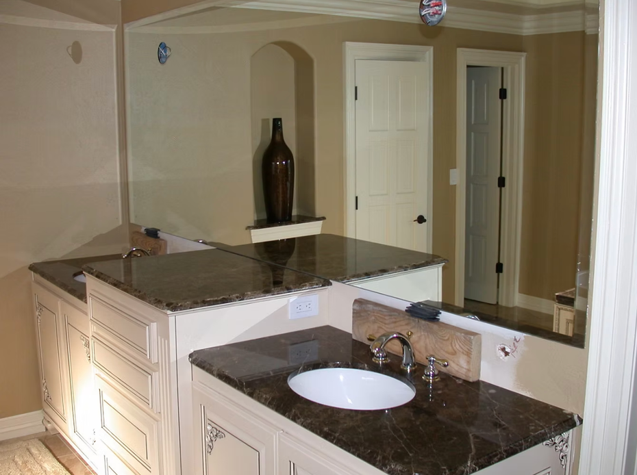 Bathroom vanity with dark granite counters, double sinks, and a large wall mirror