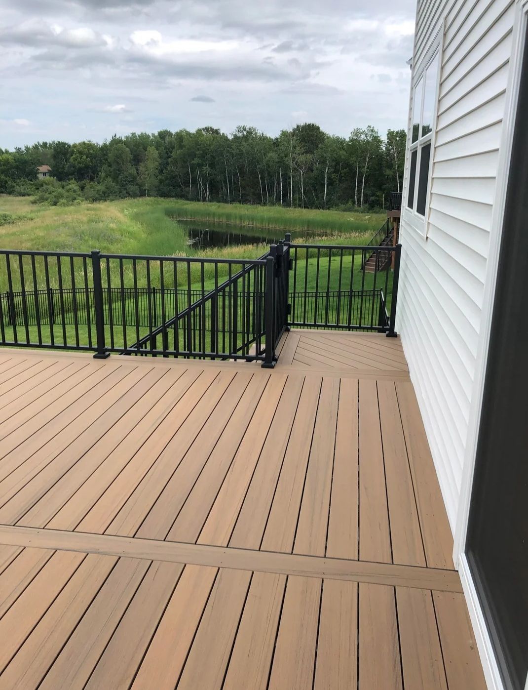 A wooden deck with a black railing and a view of a field.