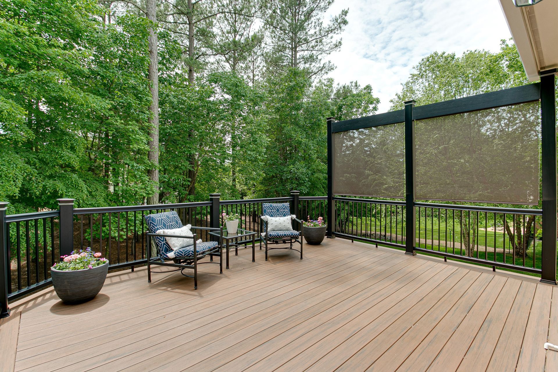 A large wooden deck with chairs and a table surrounded by trees.