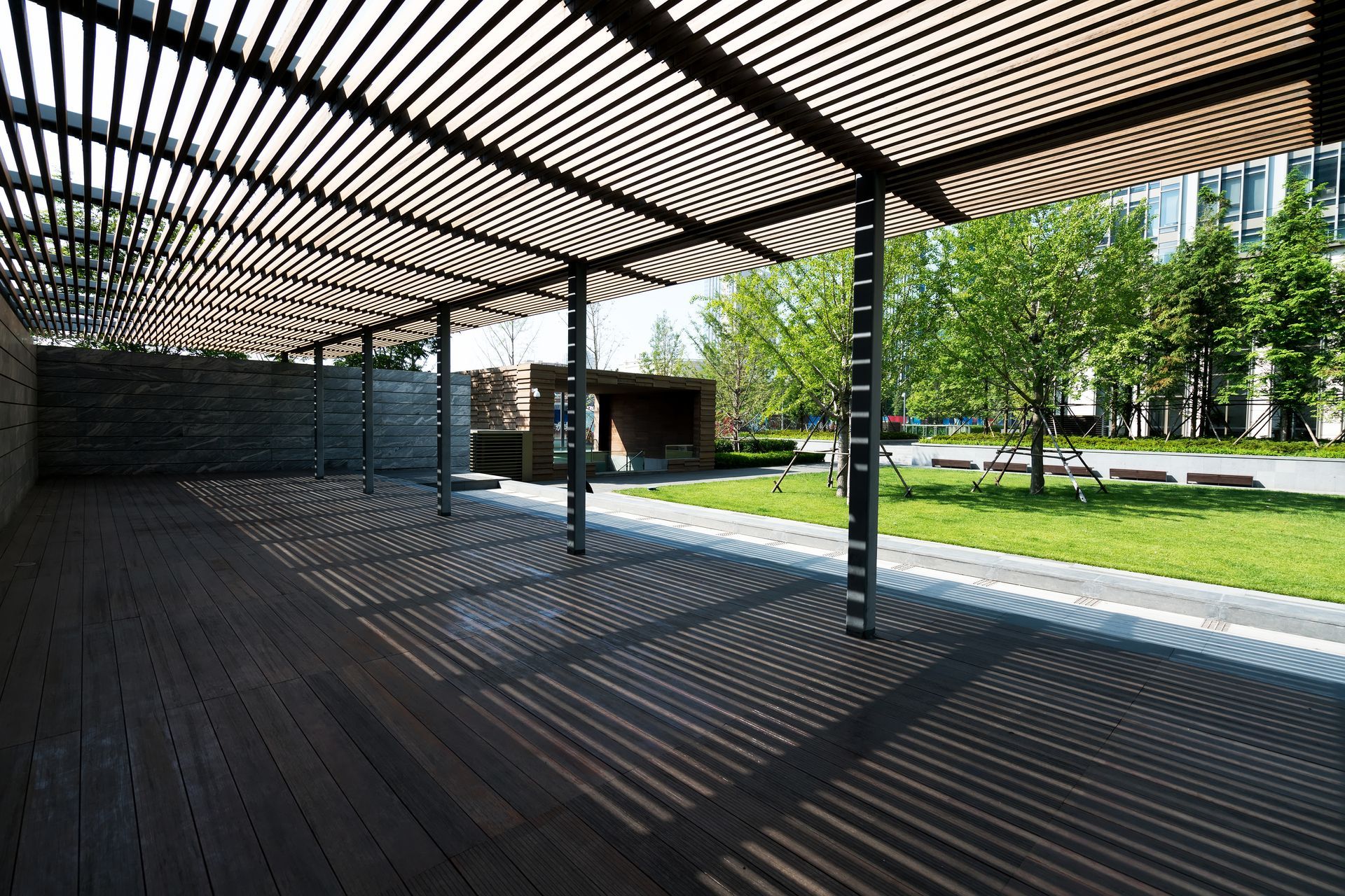 A wooden deck under a pergola with trees in the background.