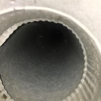 Gros plan sur l'ouverture d'un tuyau cylindrique en métal gris, à l'intérieur sombre et au bord extérieur nervuré.