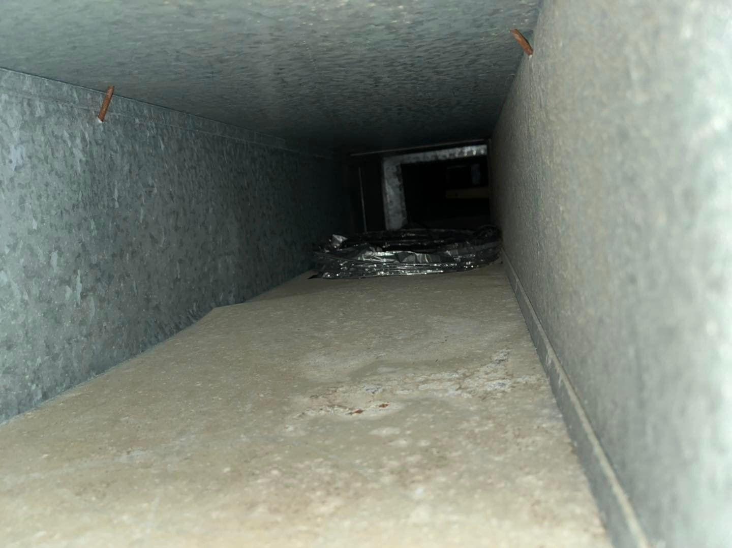 À l'intérieur d'une gaine d'aération métallique, on aperçoit un long tunnel de ventilation étroit rempli de poussière et de débris.