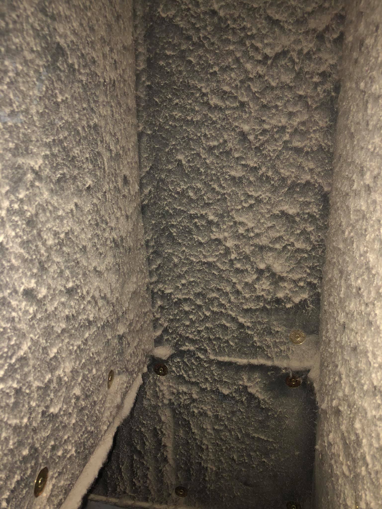 Gros plan sur un mur gris texturé et rugueux, avec un coin sombre et un petit trou près du bas.