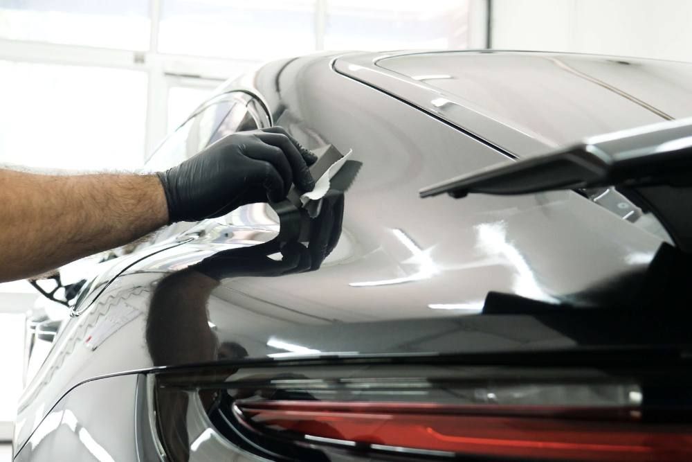 A man wearing black gloves is polishing the roof of a car.