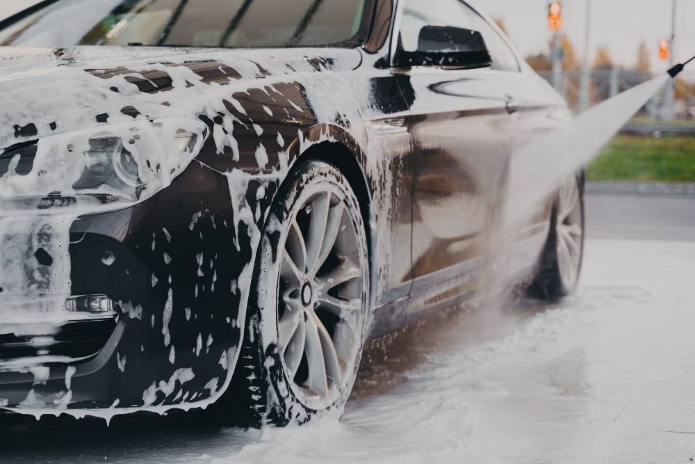 A black car is covered in foam at a car wash.