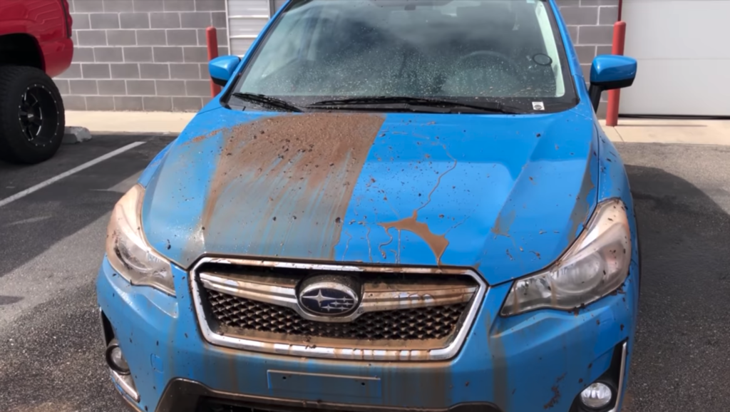 A dirty blue subaru is parked in a parking lot.