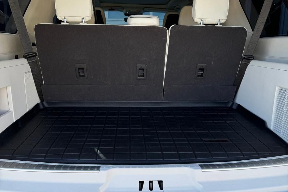 The back of a white suv with a black trunk mat.