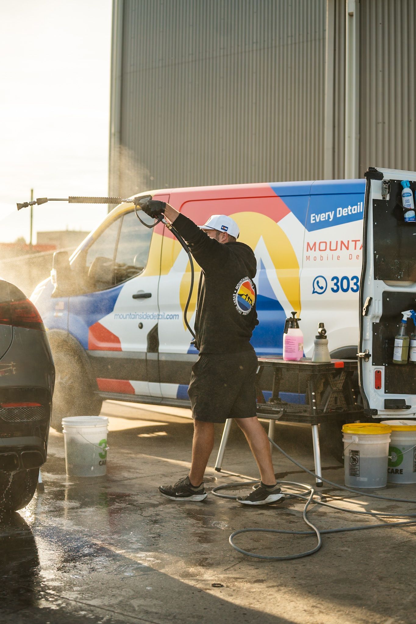 Person washing a colorful van with a hose outside a garage