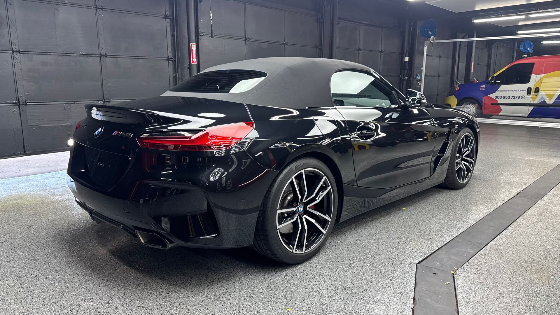 Black convertible sports car displayed indoors in a showroom, rear three-quarter view