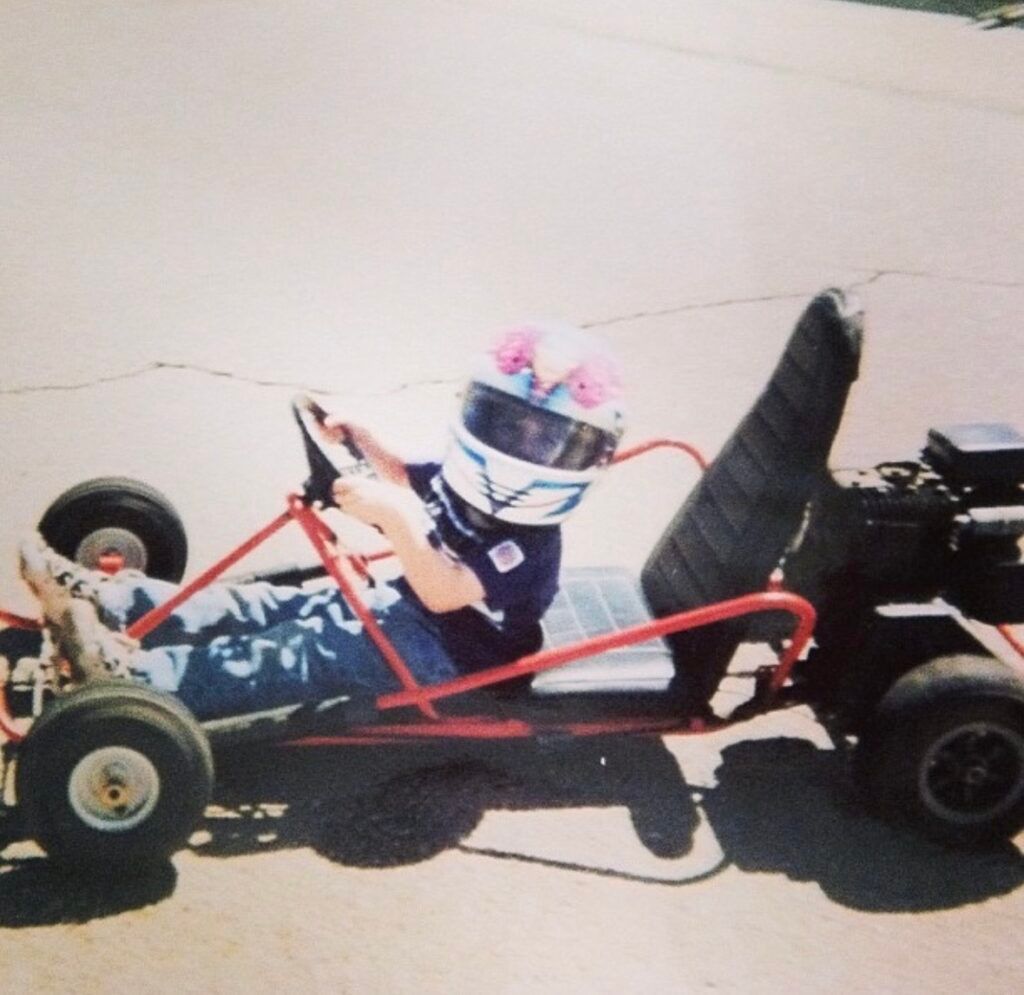 Person in a go-kart wearing a helmet, sitting on asphalt. The go-kart is red.