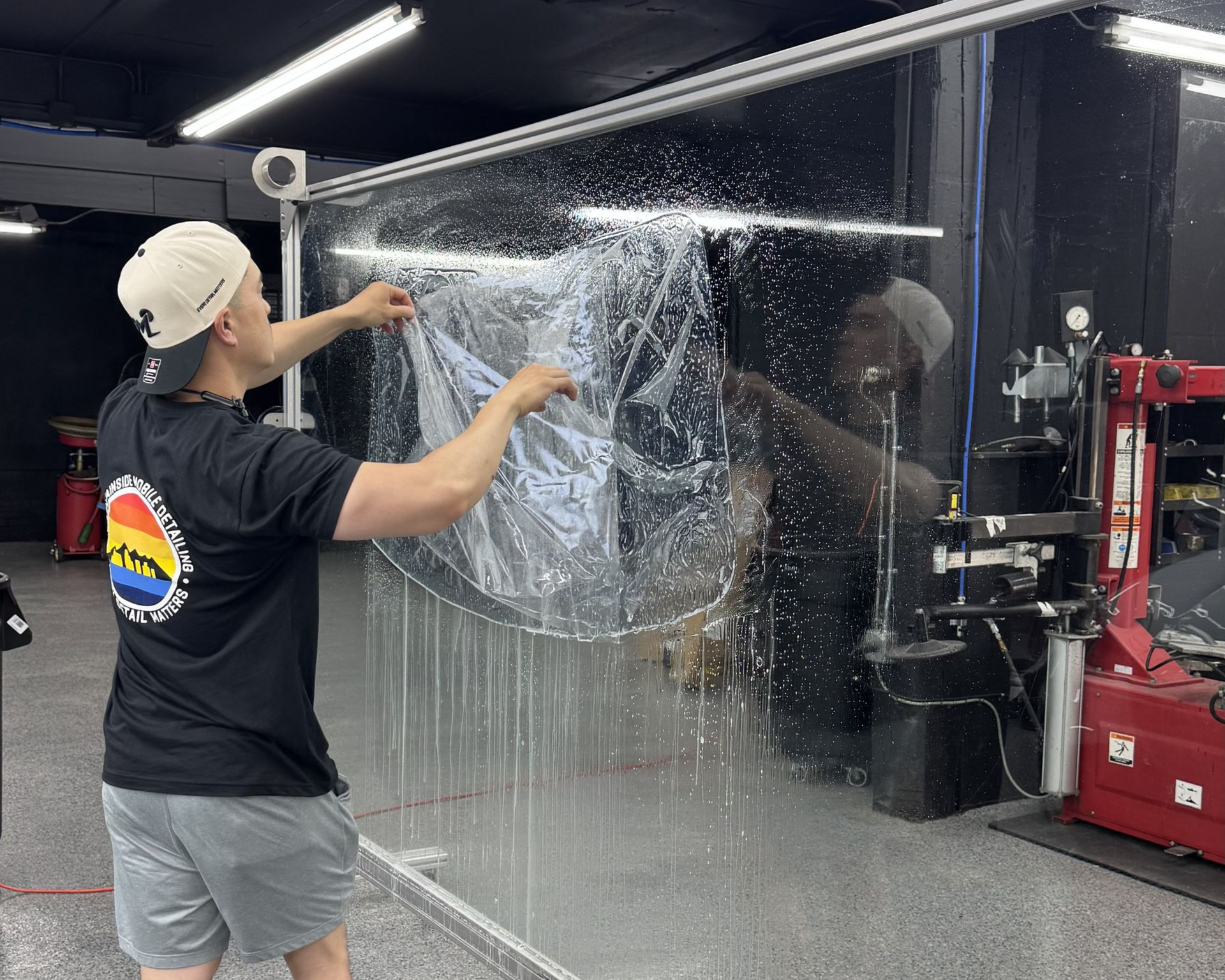Person squeegeeing water off a large clear panel in a workshop garage